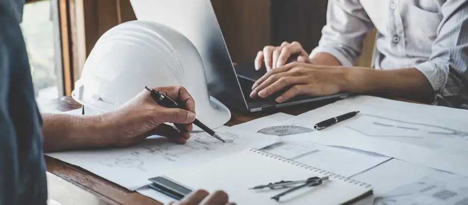 Designers reviewing technical drawings beside a hard hat