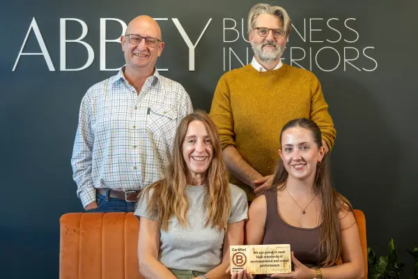 The Abbey Business Interiors team holding their Certified B Corporation plaque