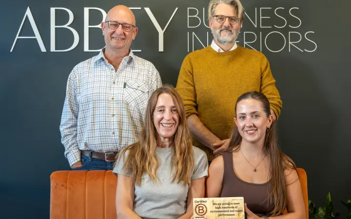 The Abbey Business Interiors team holding their Certified B Corporation plaque