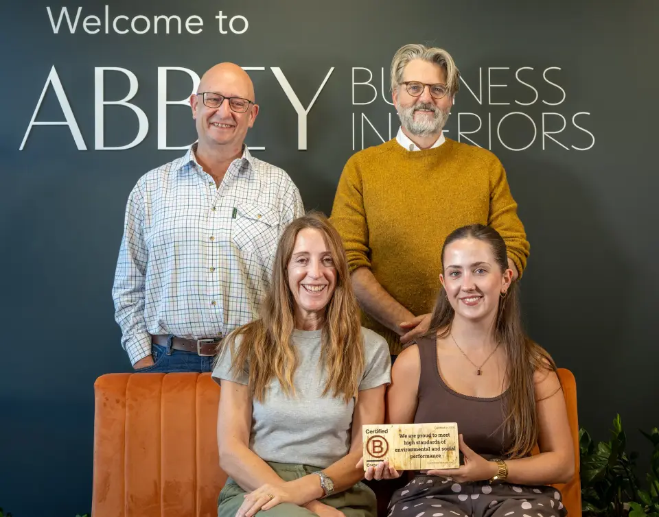 The Abbey Business Interiors team holding their Certified B Corporation plaque